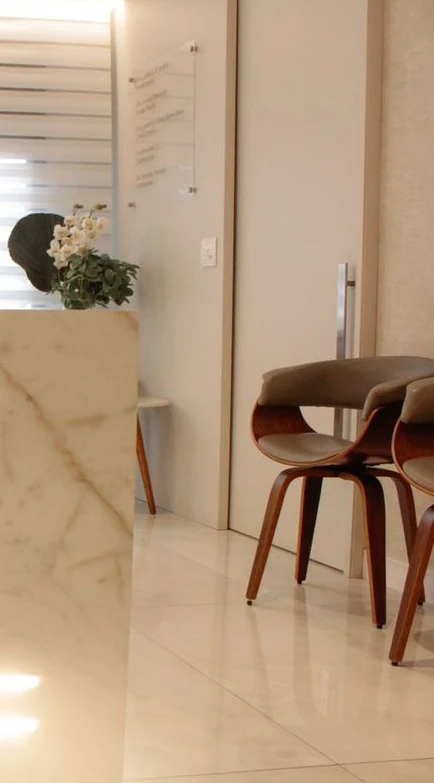 Recepção do consultório: o balcão de mármore com uma orquídea branca, a porta e as cadeiras de nogueira